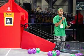 Man with microphone next do DECODE Presented by RTX playing field at the FIRST Championship. 