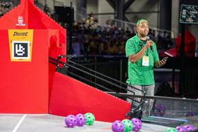 Man with microphone next do DECODE Presented by RTX playing field at the FIRST Championship. 